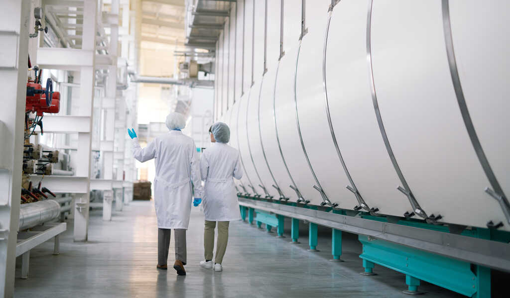 Two people walking across a manufacturing plant floor describing their services to their Marketing Consultancy team member.