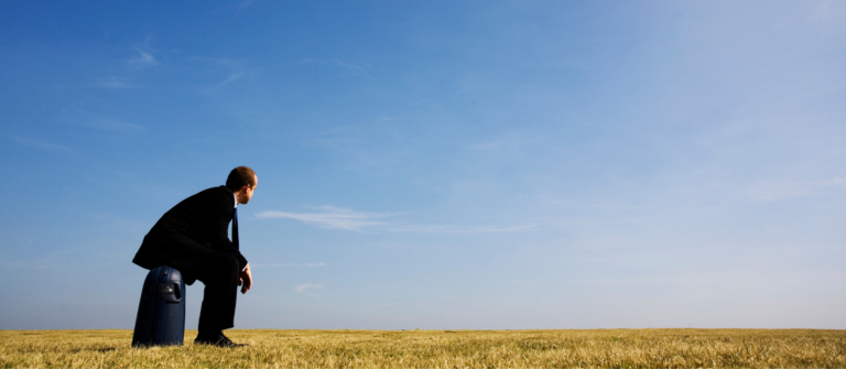 A man sitting on a suitcase in an open field represents the possibilities of working with AI agents to help B2B buyers with self-research.