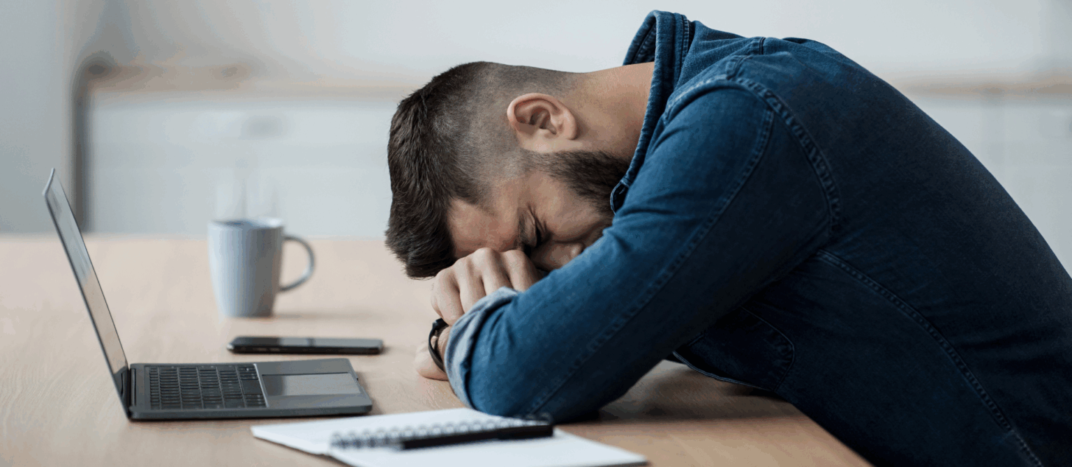 A photo of a man slumped over his desk represents the frustration of making avoidable website mistakes.