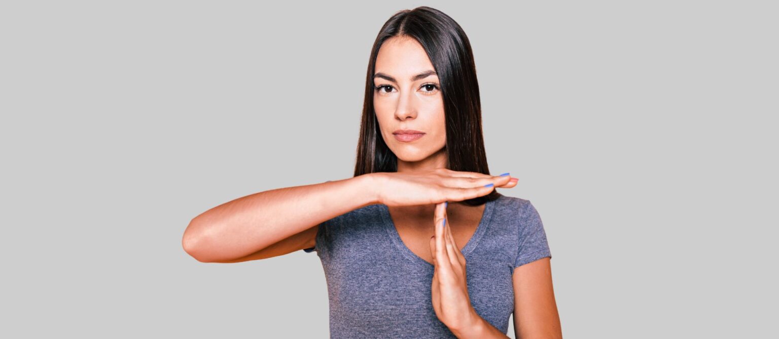 A photo of a woman making a time-out gesture represents the need to stop making your B2B landing pages all about you.