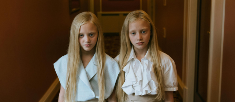 Twin girls in matching pale outfits stand side by side in a dim hallway, representing two myths about AI and critical thinking.