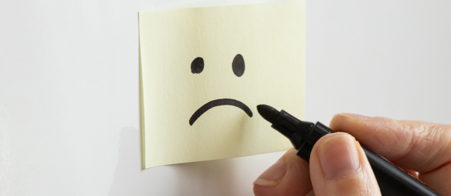 Hand drawing a sad face on a sticky note, illustrating the growing perception of marketing as a cost center.