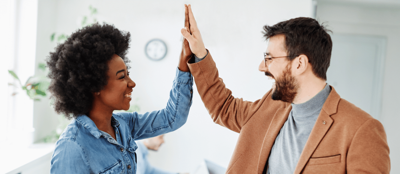 Two smiling co-workers exchange a high-five, celebrating teamwork. A streamlined legacy content review process helps marketers and experts collaborate.